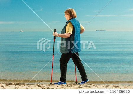 Senior woman practicing nordic walking on beach Senior woman practicing nordic walking on beach 116486650