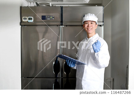 A man wearing sanitary clothing poses in the kitchen 116487266