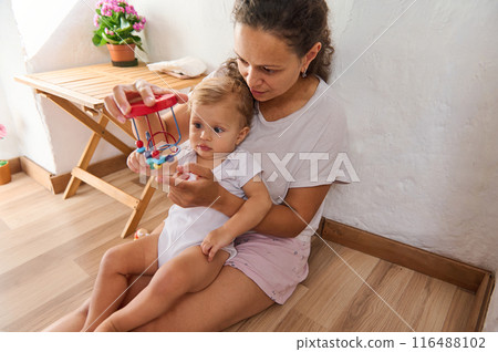 Mother and baby playing with a toy at home. Mom teaching and bonding with her child. Mother and baby playing with a toy at home. Mom teaching and bonding with her child. 116488102
