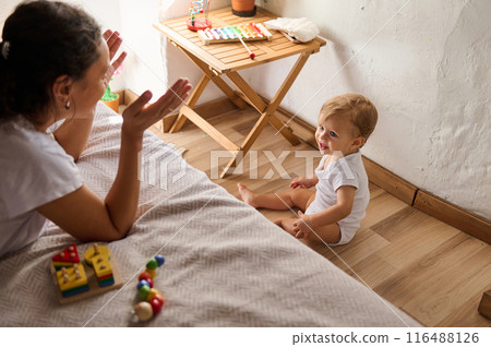 Mother playing with her baby on the floor of a cozy room filled with colorful toys Mother playing with her baby on the floor of a cozy room filled with colorful toys 116488126