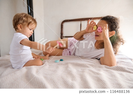 Mother and toddler playing with toys in a cozy bedroom environment, enjoying playful bonding moments Mother and toddler playing with toys in a cozy bedroom environment, enjoying playful bonding moments 116488136