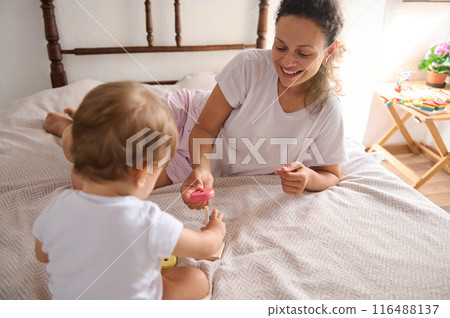 Mother playing on bed with toddler in cozy room, sharing happy moments Mother playing on bed with toddler in cozy room, sharing happy moments 116488137