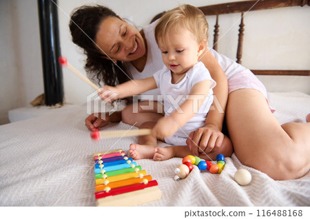Mother and toddler playing with colorful xylophone on bed, joyful moments of parenting and early learning 116488168