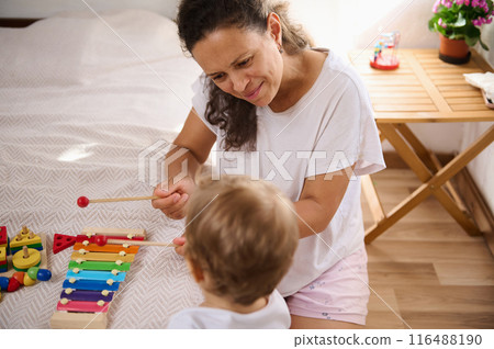 Mother and child enjoying quality time playing with colorful xylophone in cozy home 116488190