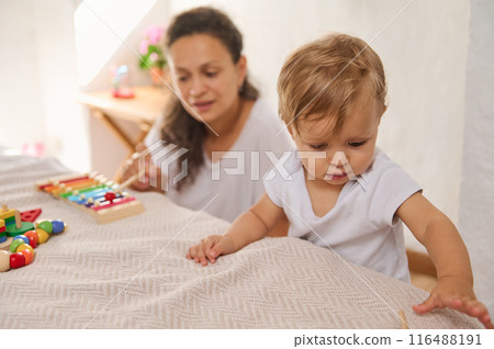 Mother and baby bonding time while playing with colorful toys in a warm home environment 116488191