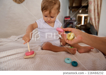 Adorable toddler playing with educational toy while sitting on bed at home 116488232