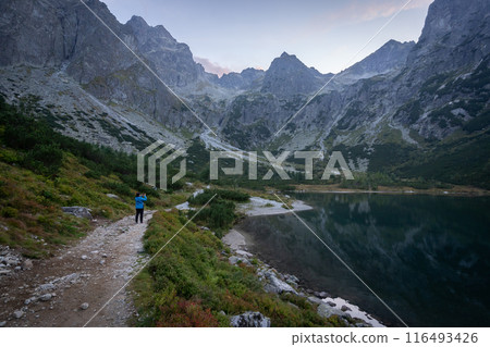 Tourist taking photos on a bank of alpine lake surrounded by mountains during sunset in Slovakia Tourist taking photos on a bank of alpine lake surrounded by mountains during sunset in Slovakia 116493426