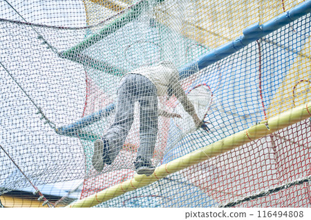 An unrecognizable girl overcoming a rope obstacle course on a playground in an open space. With space to copy. High quality photo 116494808