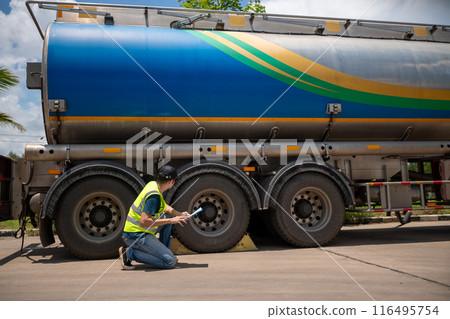 A man is kneeling down next to a large blue and green tanker truck A man is kneeling down next to a large blue and green tanker truck 116495754