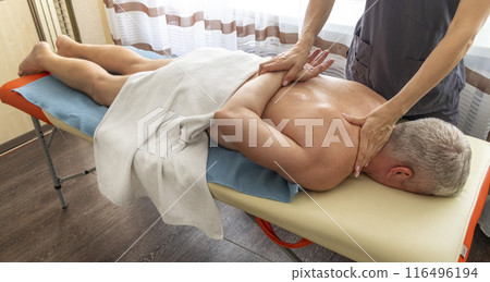 Female manual therapist performing physical therapy on mid aged male patient. Female manual therapist performing physical therapy on mid aged male patient. 116496194