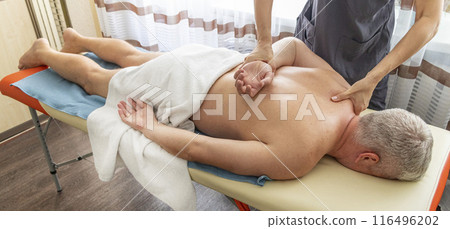 Female manual therapist performing physical therapy on mid aged male patient. Female manual therapist performing physical therapy on mid aged male patient. 116496202
