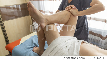 Female manual therapist performing physical therapy on mid aged male patient. 116496211