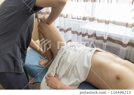 Female manual therapist performing physical therapy on mid aged male patient. Female manual therapist performing physical therapy on mid aged male patient. 116496213
