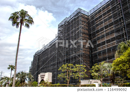 A large apartment building covered with scaffolding pipes and mesh sheets as a safety measure during large-scale repair work A large apartment building covered with scaffolding pipes and mesh sheets as a safety measure during large-scale repair work 116499092