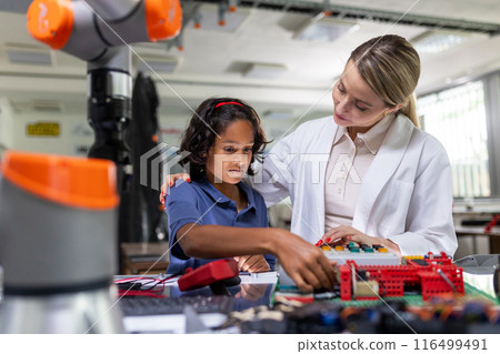 Female teacher helping young schoolboy to build robot kit in after-school robotics club. Children learning robotics in Elementary school. Science for kids. 116499491