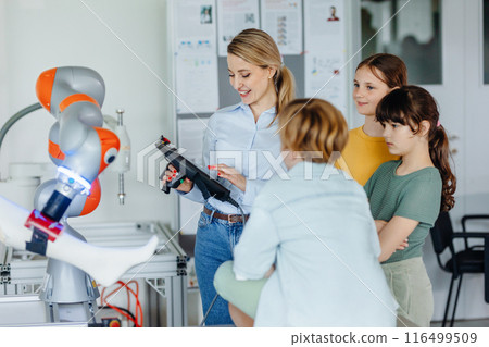 Field trip to real robotics laboratory, encouraging children in career in robotics. Real scientist talking with young students, showing them robotic arm. Field trip to real robotics laboratory, encouraging children in career in robotics. Real scientist talking with young students, showing them robotic arm. 116499509