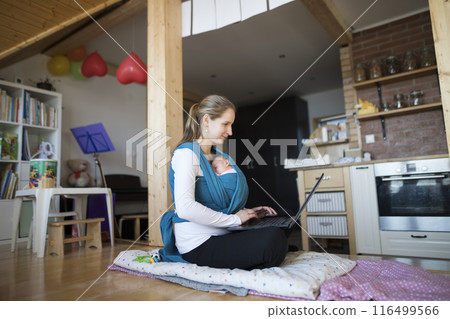 Newborn baby sleeping in baby sling, wrap, mother typing on laptop. Unconditional paternal love, mother's Day. Newborn baby sleeping in baby sling, wrap, mother typing on laptop. Unconditional paternal love, mother's Day. 116499566