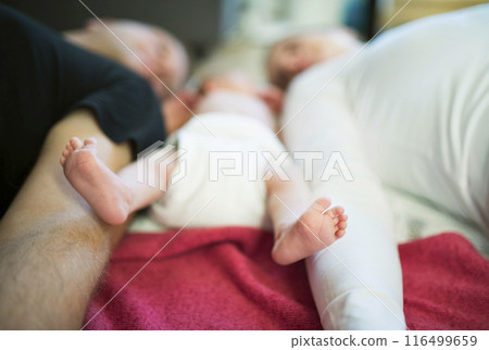 New parents lying on bed by newborn baby girl. Unconditional paternal love, idyllic family moment. 116499659