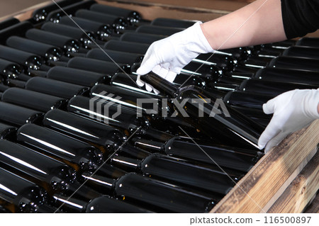 A bottle of wine in his hands. Hands in white gloves. The new wine is stored. Bottled wine at the winery A bottle of wine in his hands. Hands in white gloves. The new wine is stored. Bottled wine at the winery 116500897