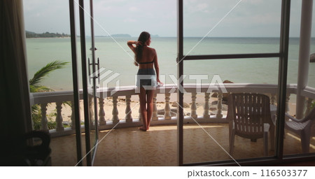 Woman relax standing on a balcony of a resort in Thailand, gazes out at the peaceful ocean. Tropic nature coastline landscape in background. Female tourist on summer vacation. Lifestyle holiday 116503377