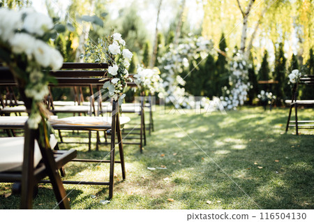 Wooden chairs decorated with flowers for an outdoor wedding ceremony 116504130