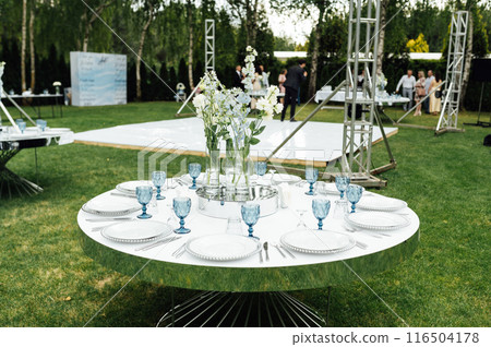 Wedding in an open space. Guest tables are decorated with fresh flowers and premium glasses Wedding in an open space. Guest tables are decorated with fresh flowers and premium glasses 116504178