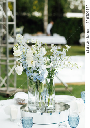 Wedding in an open space. Guest tables are decorated with fresh flowers and premium glasses Wedding in an open space. Guest tables are decorated with fresh flowers and premium glasses 116504183