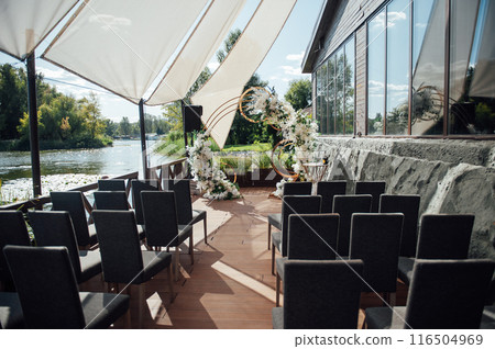 Modern area for an outdoor ceremony. Round arch with dark chairs for guests and a sun canopy Modern area for an outdoor ceremony. Round arch with dark chairs for guests and a sun canopy 116504969