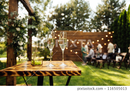 Elegant glasses of champagne for the newlyweds stand on the table next to the ceremony arch Elegant glasses of champagne for the newlyweds stand on the table next to the ceremony arch 116505013