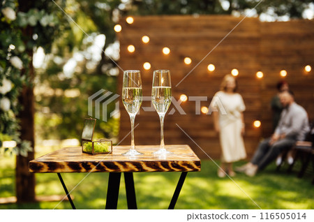 Elegant glasses of champagne for the newlyweds stand on the table next to the ceremony arch Elegant glasses of champagne for the newlyweds stand on the table next to the ceremony arch 116505014