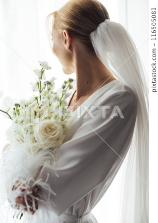 The morning of the bride, a woman wearing a white silk robe holds a wedding bouquet. Close-up photo. The morning of the bride, a woman wearing a white silk robe holds a wedding bouquet. Close-up photo. 116505081