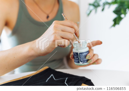 young woman draws picture on clothes with paints, handmade craft work. Customization young woman draws picture on clothes with paints, handmade craft work. Customization 116506855