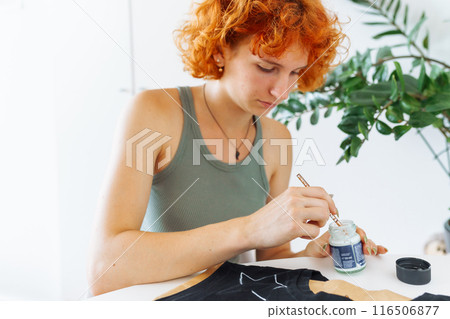 young woman draws picture on clothes with paints, handmade craft work. Customization 116506877