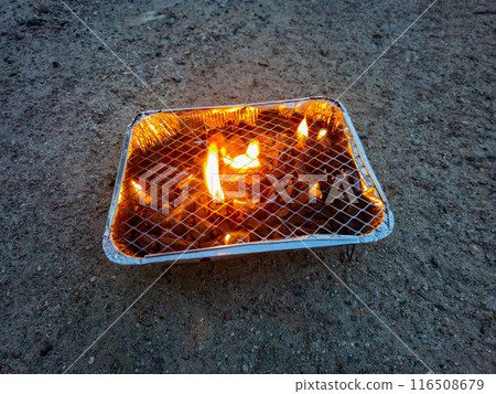 Lighting the disposable grill on the ground. 116508679