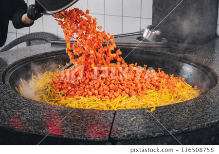 male chef roasts carrots in cauldron to cook traditional Uzbek pilaf in kitchen at restaurant in Uzbekistan 116508758