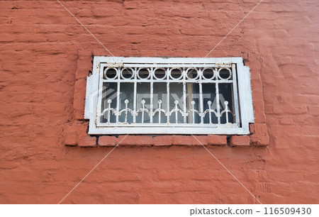 On the red brick facade there is a small rectangular window with a white wrought-iron grille 116509430