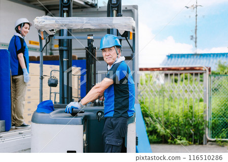 戴頭盔的工人用堆高機將貨物裝載到卡車上 116510286