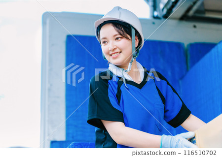 A female driver wearing a helmet riding on the back of a truck 116510702