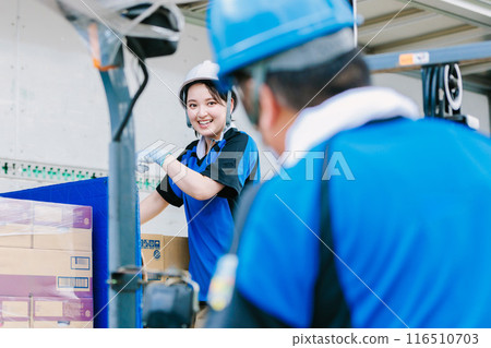 A worker in a helmet loading cargo onto a truck with a forklift A worker in a helmet loading cargo onto a truck with a forklift 116510703