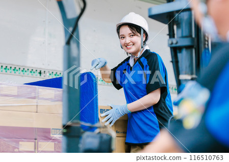 A worker in a helmet loading cargo onto a truck with a forklift A worker in a helmet loading cargo onto a truck with a forklift 116510763