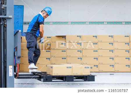 A man in a helmet unloading cargo from a truck with a forklift 116510787