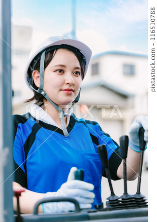 A woman in a helmet driving a forklift 116510788