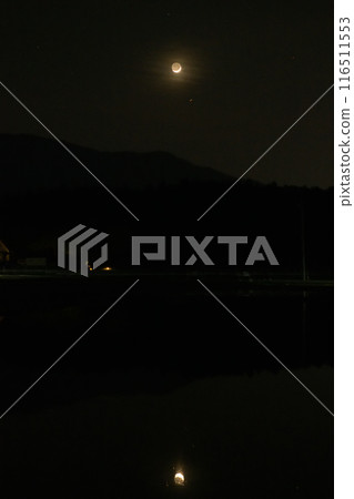 A crescent moon in the evening sun reflected on a rice field that has been plowed and is waiting to be planted in Hakushu Town, Hokuto City 116511553