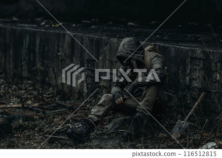 A man in dark green camouflage and a gas mask sits among the ruins of the city. A man in dark green camouflage and a gas mask sits among the ruins of the city. 116512815