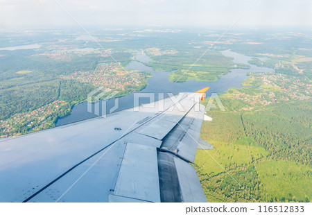 View of airplane wing, blue skies and green land during landing. Airplane window view. 116512833