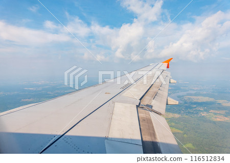 View of airplane wing, blue skies and green land during landing. Airplane window view. 116512834
