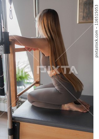 Calm and peaceful woman resting after training in pilates studio. A woman is engaging in a Pilates exercise session using Pilates equipment  116515053