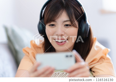 A woman lying on the sofa watching videos on her smartphone A woman lying on the sofa watching videos on her smartphone 116516130
