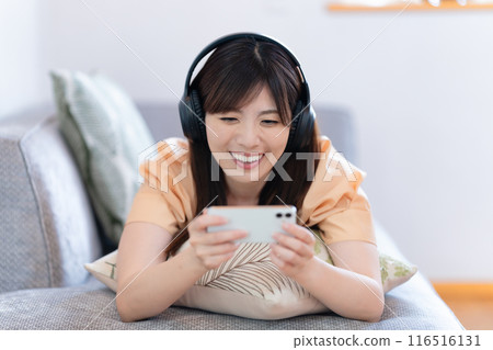 A woman lying on the sofa watching videos on her smartphone 116516131