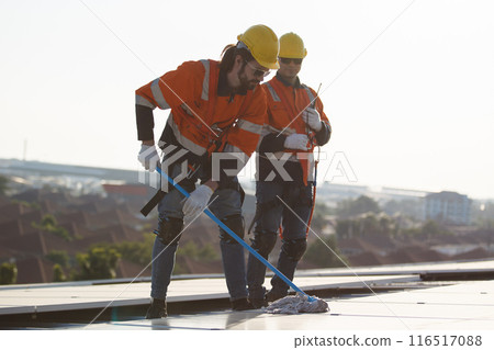 Professional electrical engineers working on the residential rooftop to clean up the dusty solar panels. 116517088